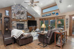 Living room with high vaulted ceiling, a stone fireplace, wood finished floors, and a ceiling fan