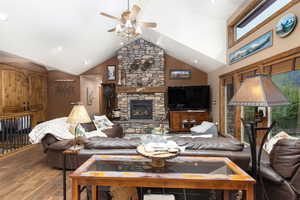 Living area featuring a stone fireplace, high vaulted ceiling, wood finished floors, ceiling fan, and recessed lighting