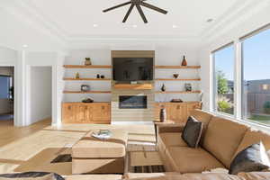 Living area with ceiling fan, a large fireplace, recessed lighting, a raised ceiling, and light wood-style flooring