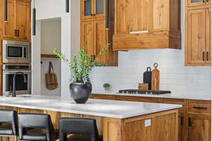 Kitchen with brown cabinets, glass insert cabinets, appliances with stainless steel finishes, and premium range hood
