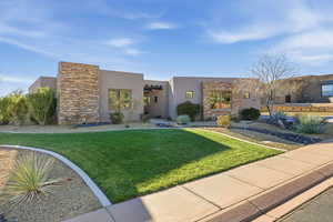 View of front facade featuring stone siding, a front lawn, and stucco siding