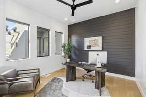 Office area with an accent wall, ceiling fan, wood walls, light wood-style floors, and recessed lighting