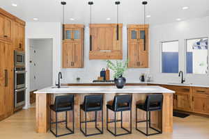 Kitchen featuring brown cabinetry, a kitchen bar, a center island with sink, decorative light fixtures, and recessed lighting