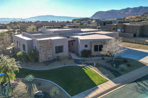 Pueblo revival-style home featuring stucco siding, a mountain view, stone siding, and a front lawn