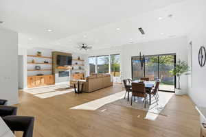 Dining space featuring light wood-type flooring, a ceiling fan, a glass covered fireplace, recessed lighting, and a tray ceiling