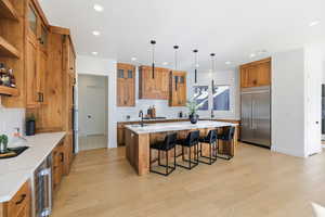 Kitchen featuring brown cabinetry, a kitchen island with sink, a kitchen breakfast bar, decorative light fixtures, and recessed lighting