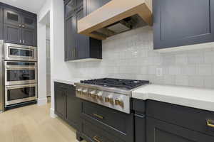 Kitchen featuring custom range hood, stainless steel appliances, light wood-type flooring, glass insert cabinets, and decorative backsplash