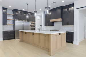 Kitchen with glass insert cabinets, open shelves, built in appliances, tasteful backsplash, and light wood-type flooring