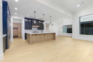Kitchen featuring a large island, light wood-type flooring, glass insert cabinets, pendant lighting, and recessed lighting