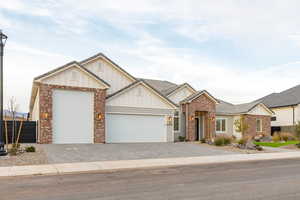 View of front of house with board and batten siding, a garage, decorative driveway, and brick siding