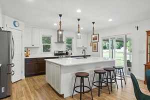 Kitchen with white cabinetry, appliances with stainless steel finishes, wall chimney range hood, a kitchen breakfast bar, and decorative light fixtures
