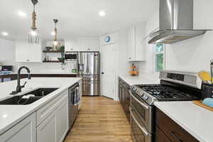 Kitchen with white cabinetry, stainless steel appliances, ventilation hood, decorative light fixtures, and recessed lighting