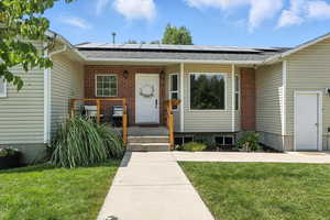 Property entrance featuring a yard, brick siding, solar panels, and a shingled roof