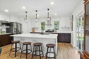 Kitchen featuring white cabinets, decorative light fixtures, recessed lighting, wall chimney range hood, and a kitchen breakfast bar