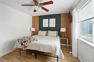 Bedroom with light wood-type flooring, a ceiling fan, attic access, and an accent wall