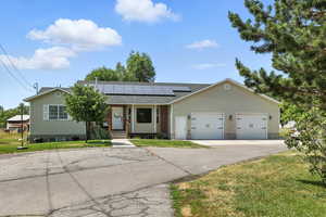Ranch-style house with solar panels, a front lawn, an attached garage, driveway, and a porch