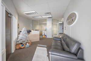 Carpeted living area with a paneled ceiling and a desk