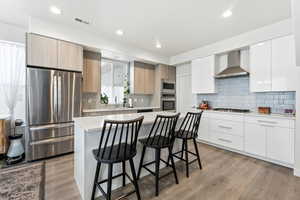 Kitchen featuring appliances with stainless steel finishes, modern cabinets, a breakfast bar area, wall chimney exhaust hood, and recessed lighting