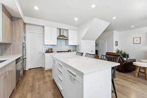 Kitchen with a kitchen bar, modern cabinets, light stone counters, white cabinetry, and light wood-style flooring