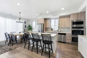 Kitchen featuring decorative light fixtures, a kitchen island, a breakfast bar area, stainless steel appliances, and tasteful backsplash