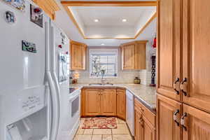 Kitchen with white appliances, a tray ceiling, decorative backsplash, stone tile floors, and recessed lighting