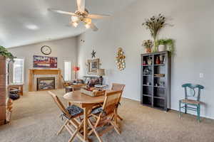 Dining room featuring light carpet, a fireplace, a ceiling fan, and high vaulted ceiling