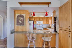 Kitchen with light stone countertops, backsplash, white appliances, recessed lighting, and a breakfast bar