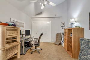 Office/bedroom area with light carpet, ceiling fan, and high vaulted ceiling