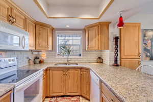 Kitchen featuring white appliances, a raised ceiling, light stone counters, tasteful backsplash, and pendant lighting