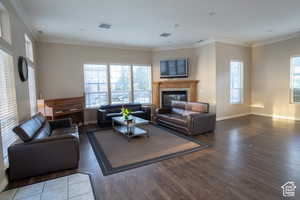 Living area with crown molding, a glass covered fireplace, and dark wood-style floors
