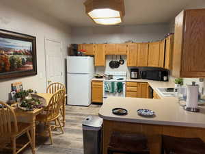 Kitchen with black appliances, light countertops, light wood-type flooring, a peninsula, and a breakfast bar