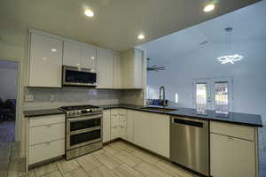 Kitchen with stainless steel appliances, white cabinetry, dark stone counters, vaulted ceiling, and decorative backsplash