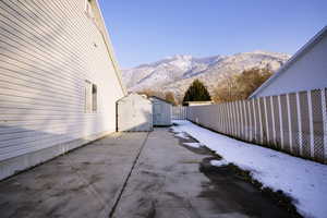 Snow covered patio with a storage shed, a mountain view, a patio, and a fenced backyard