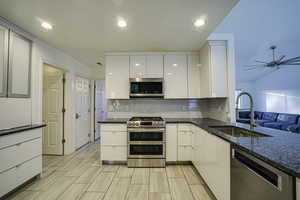 Kitchen with appliances with stainless steel finishes, dark stone countertops, backsplash, white cabinets, and recessed lighting