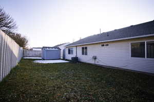 Rear view of house featuring a storage unit, a patio area, a fenced backyard, and a shingled roof