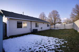 Snow covered rear of property featuring a fenced backyard and roof with shingles