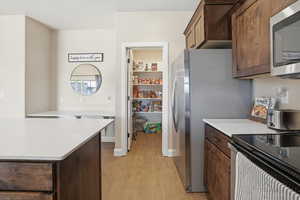 Kitchen featuring dark brown cabinets, stainless steel appliances, light wood-type flooring, and light stone counters