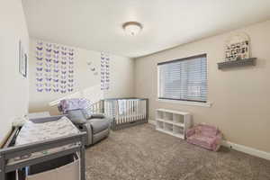 Carpeted bedroom featuring a crib and baseboards