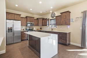 Kitchen featuring stainless steel appliances, dark brown cabinets, a kitchen island, recessed lighting, and light stone countertops