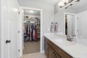 Bathroom featuring a walk in closet, vanity, and light colored carpet