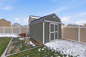 Snow covered structure with a fenced backyard and a storage unit