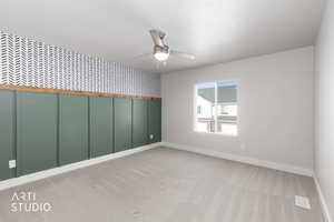 Unfurnished room featuring wallpapered walls, ceiling fan, light carpet, and a wainscoted wall