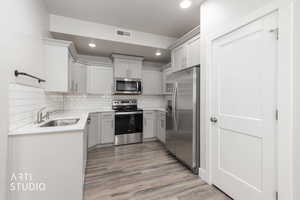 Kitchen with stainless steel appliances, light wood-style flooring, light stone countertops, backsplash, and gray cabinetry
