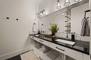 Bathroom with double vanity, backsplash, and dark tile patterned floors