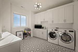 Washroom featuring cabinet space, washer and clothes dryer, light floors, and a chandelier