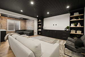 Cinema room with brick wall, recessed lighting, light wood-style floors, wood ceiling, and bar with sink