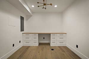 Unfurnished office with built in desk, dark wood-style floors, electric panel, and recessed lighting