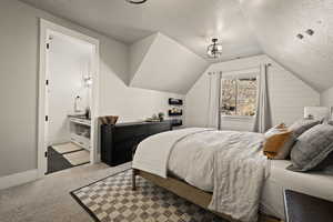 Carpeted bedroom featuring a textured ceiling, lofted ceiling, and ensuite bath