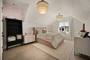 Bedroom featuring vaulted ceiling, wood finished floors, a textured ceiling, and wallpapered walls