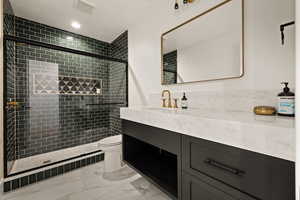 Bathroom featuring vanity, a tile shower, light marble finish floors, and recessed lighting